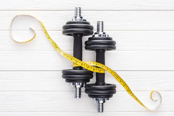 Top view of dumbbells and yellow measuring tape on wooden surface — Stock Photo