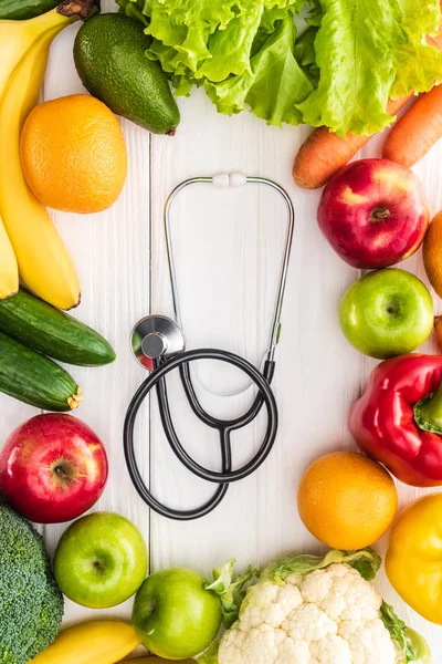 Top view of fresh fruits and vegetables and stethoscope on wooden table — Stock Photo