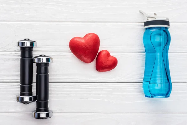 Top view of dumbbells, bottle of water and red hearts on wooden surface — Stock Photo
