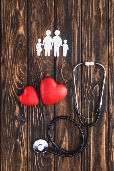 Вид зверху на білих фігур родини, що тримає руки, символи червоних сердець та стетоскоп — стокове фото