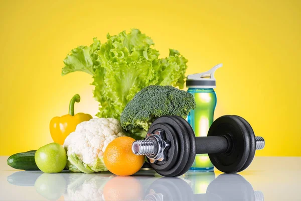 Vista close-up de haltere, garrafa de água e frutas e legumes frescos no amarelo — Fotografia de Stock