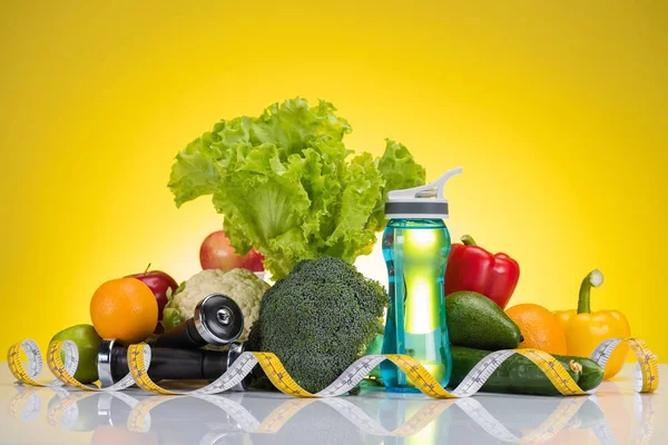 Крупним планом вид на свіжі фрукти і овочі, мірна стрічка, пляшка води і гантелі на жовтому — стокове фото