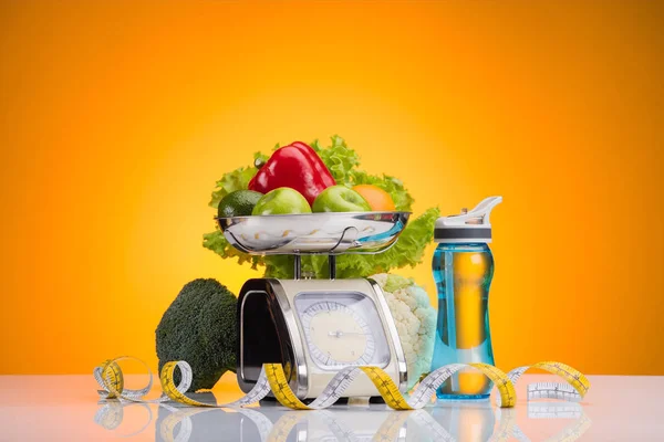 Свіжі фрукти та овочі на вагах, спортивна пляшка з водою та вимірювальна стрічка на жовтому — стокове фото