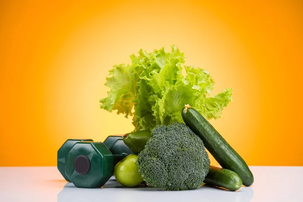 Close-up view of green dumbbells and fresh fruits and vegetables on yellow — Stock Photo