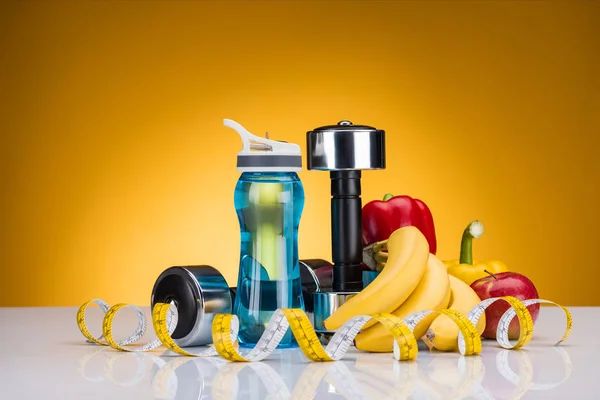 Vista ravvicinata di manubri, bottiglia d'acqua, metro a nastro e peperoni con frutta su fondo giallo — Foto stock