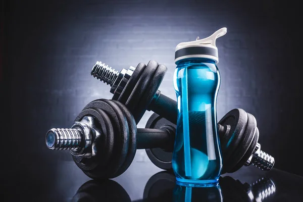 Vista de cerca de la botella de deportes llena de agua y mancuernas, deporte y estilo de vida saludable concepto - foto de stock