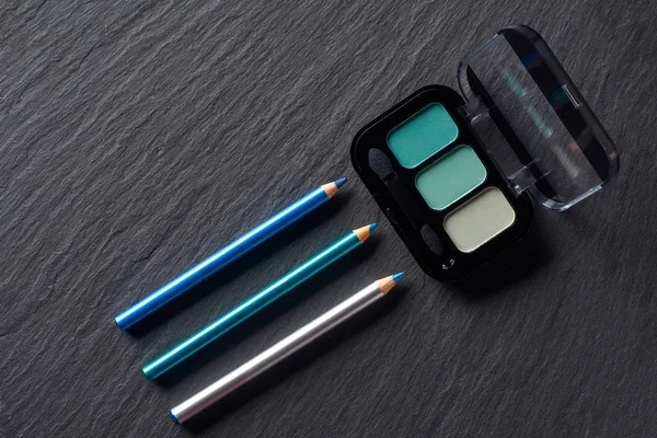 Blue eye shadows and pencils on dark slate background — Stock Photo