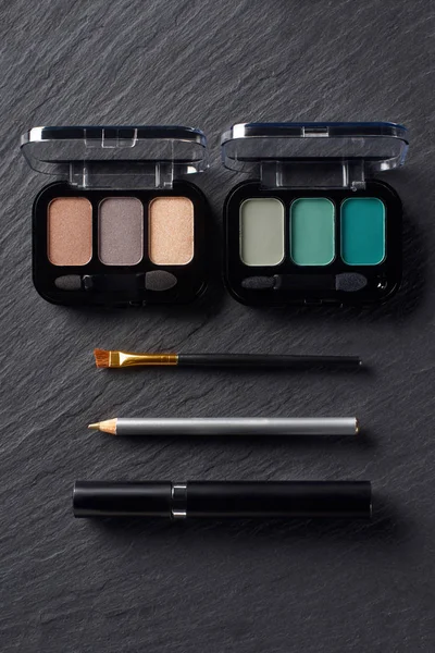 Palettes with eye shadows, pencil and mascara on dark slate background — Stock Photo