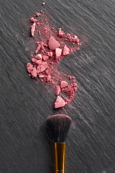 Broken blush and large brush on dark slate background — Stock Photo