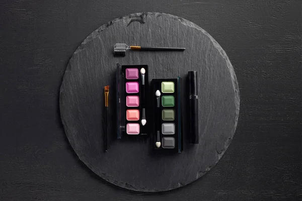 Set of eye shadows palettes with brushes on round slate background — Stock Photo