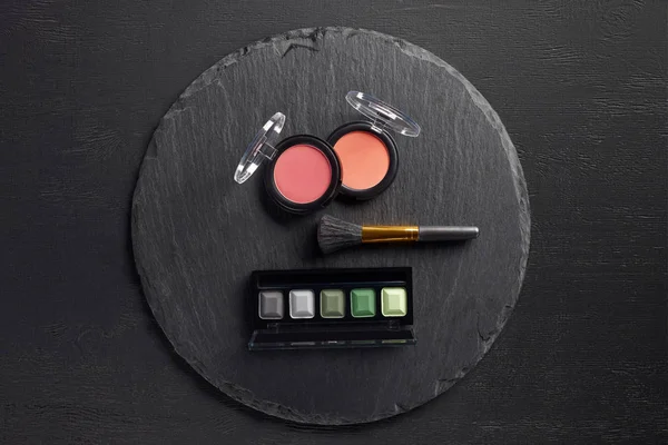 Blush and eye shadows with brush on round slate background — Stock Photo