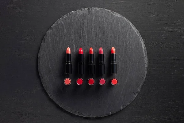 Row of red lipsticks on round slate background — Stock Photo