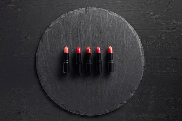 Row of lipsticks in pink and red tones on round slate background — Stock Photo