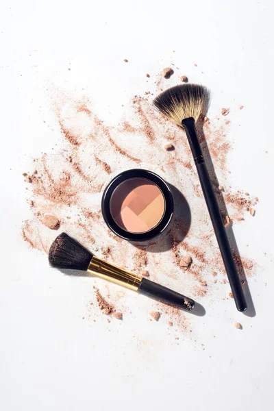 Pressed contouring powder with brushes on white background with scattered foundation — Stock Photo