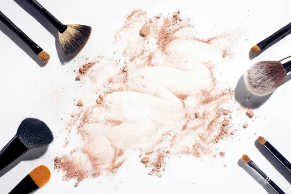 Frame of makeup brushes on white background with scattered face powder — Stock Photo