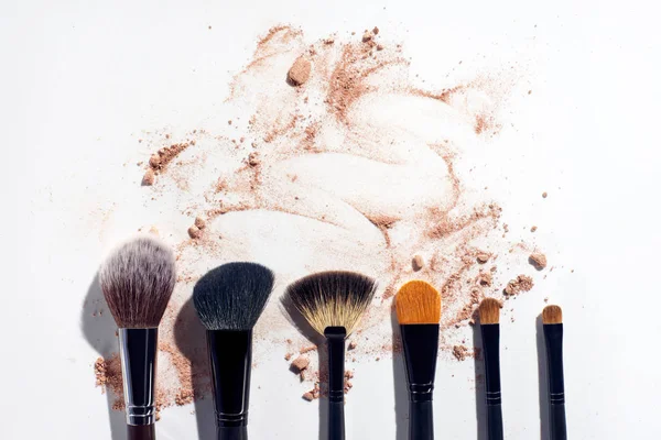 Set of brushes in a row on white background with scattered face powder — Stock Photo