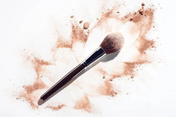 Plush makeup brush on white background with scattered face powder — Stock Photo