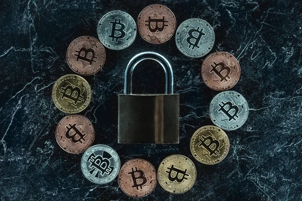 Vista superior de la cerradura arreglada y varios bitcoins en la superficie de mármol oscuro - foto de stock