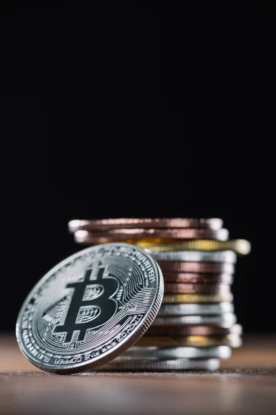 Vista de cerca de bitcoin apoyado en la pila de varios bitcoins sobre fondo negro - foto de stock