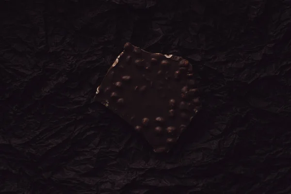 Vue du dessus du chocolat avec des morceaux de noix sur la surface recouverte de papier froissé noir — Photo de stock