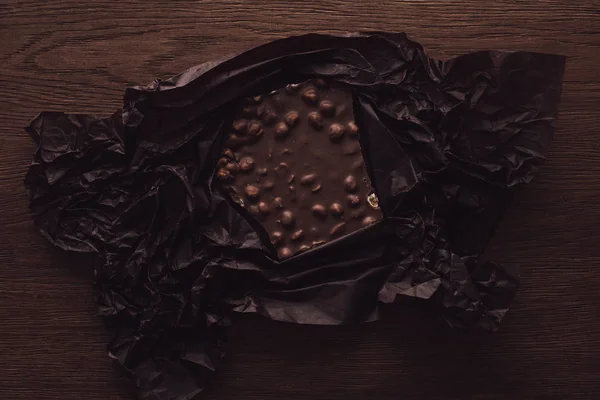 Vue du dessus du chocolat avec des noix en papier froissé noir sur table en bois — Photo de stock