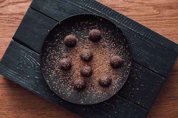Вид сверху на разделочную доску и плиту с трюфелями, покрытыми тертым шоколадом на деревянном столе — стоковое фото