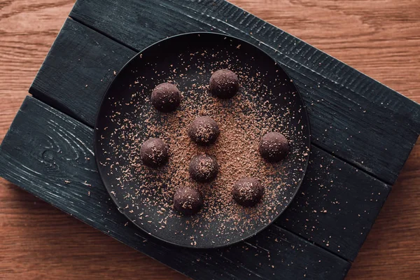 Top view of cutting board and plate with truffles covering by grated chocolate on wooden table — Stock Photo