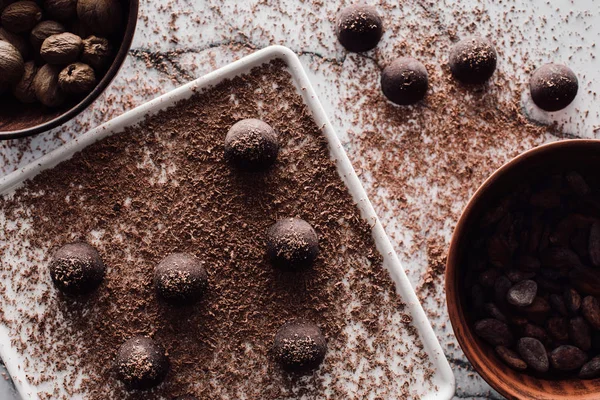 Vista superior de cuencos con nueces y granos de cacao, plato con trufas cubierta por chocolate rallado sobre mesa de mármol - foto de stock