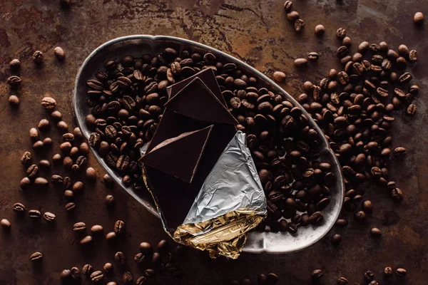 Erhöhte Ansicht von Schokolade in Folie und Kaffeebohnen in Silbertablett auf rustikalem Tisch — Stockfoto