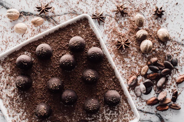Vista superior de la placa con cobertura de trufas por chocolate rallado, granos de cacao, anís y nueces en la mesa de mármol - foto de stock