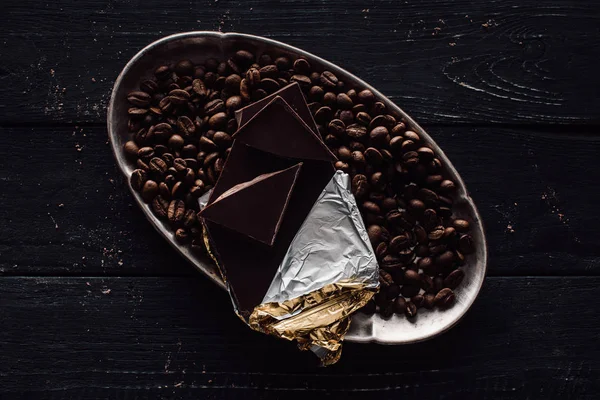 Vista elevata di cioccolato in lamina e chicchi di caffè in vassoio d'argento su tavolo di legno — Foto stock