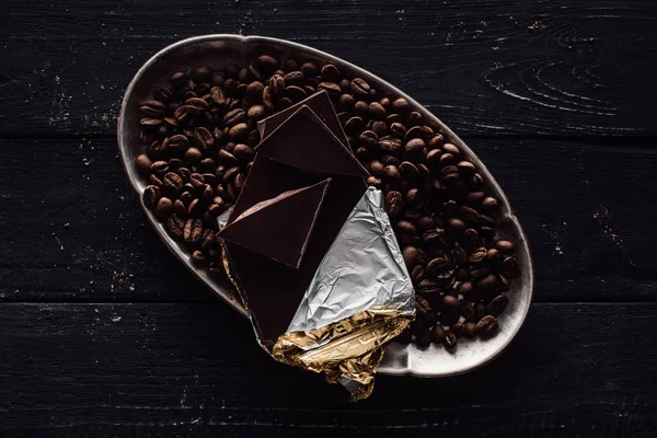 Elevated view of chocolate in foil and coffee grains in silver tray on wooden table — Stock Photo