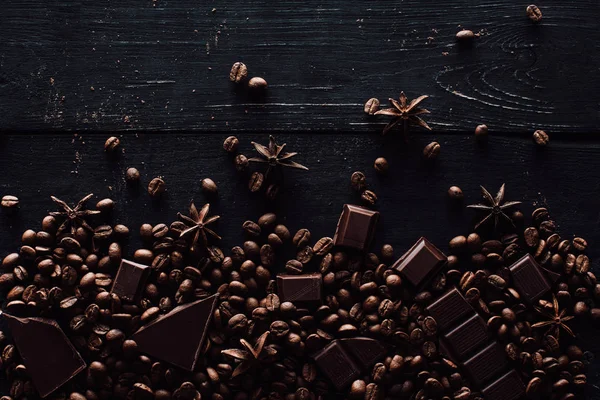 Vista elevada de anis, pedaços de chocolate e pilha de grãos de café em mesa de madeira — Fotografia de Stock