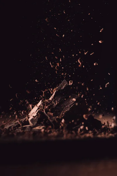 Primo piano vista di cioccolato fondente grattugiato che cade su pezzi di cioccolato su sfondo nero — Foto stock