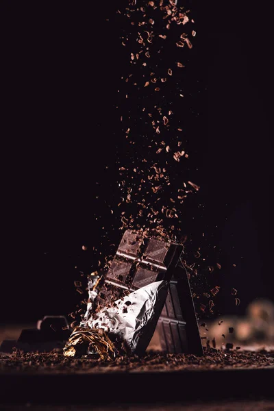 Primo piano immagine di cioccolato grattugiato che cade su due barrette di cioccolato su tavolo di legno su sfondo nero — Foto stock