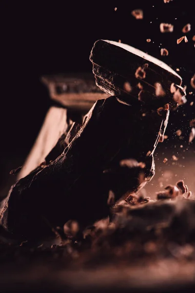 Primo piano vista di cioccolato fondente grattugiato che cade su pezzi di cioccolato su sfondo nero — Foto stock