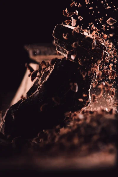 Imagem de perto de chocolate ralado caindo em pedaços de chocolate no fundo preto — Fotografia de Stock