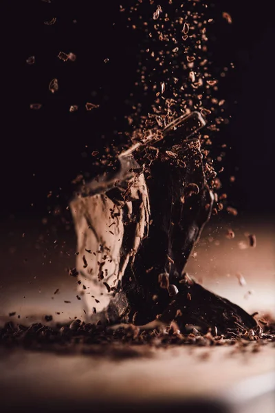 Closeup view of grated dark chocolate falling on arranged pieces of chocolate on black background — Stock Photo