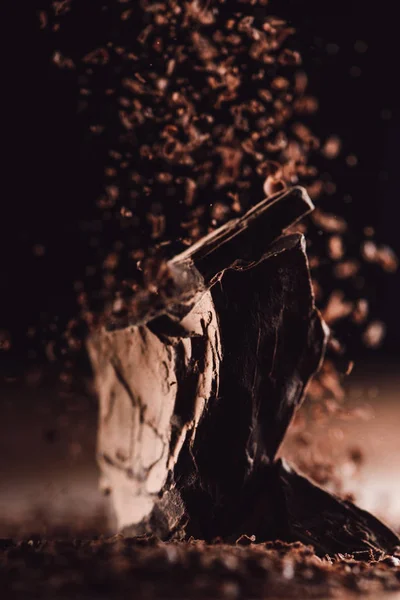 Primo piano vista di cioccolato grattugiato che cade su pezzi di cioccolato su sfondo nero — Foto stock