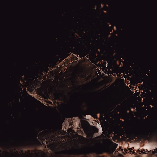 Close up shot of grated chocolate falling on arranged pieces of chocolate on black background — Stock Photo