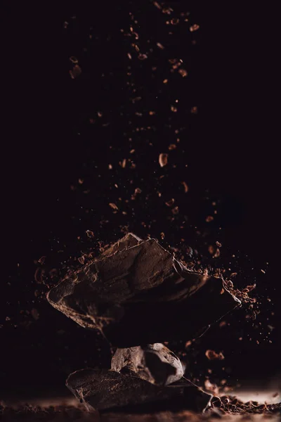 Nahaufnahme von geriebener Schokolade, die auf Schokoladenstücke auf schwarzem Hintergrund fällt — Stockfoto