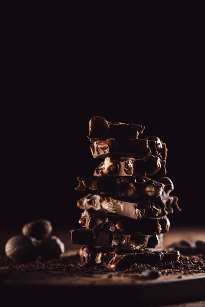 Closeup shot of stack of chocolate pieces and nutmegs on black background — Stock Photo