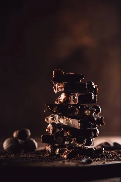 Nahaufnahme eines Stapels von Schokoladenstücken und Muskatnüssen auf einer hölzernen Tischplatte — Stockfoto