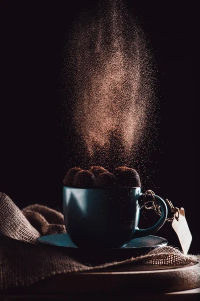 Крупным планом тертый шоколад падает на трюфели в чашке кофе на мешковину и резки доски на черном фоне — стоковое фото