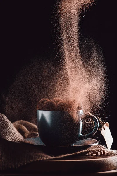 Close up tiro de chocolate ralado caindo em trufas na xícara de café em pano de saco e placa de corte em fundo preto — Fotografia de Stock