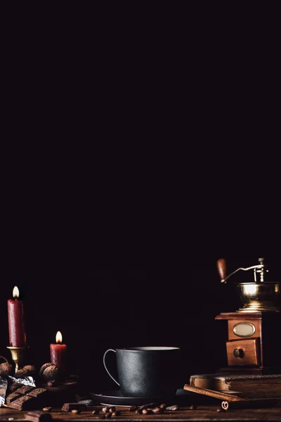 Крупним планом вид чашки кави на дерев'яному столі з шоколадом, трюфелями, зернами кави та свічками на чорному фоні — стокове фото