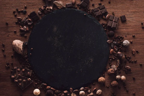 Vista sopraelevata di tagliere circondato da vari tipi di pezzi di cioccolato, tartufi. chicchi di caffè e fave di cacao sul tavolo di legno — Foto stock