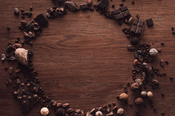 Vista superior del círculo hecho de varios tipos de piezas de chocolate, trufas, granos de café y granos de cacao en la mesa de madera - foto de stock