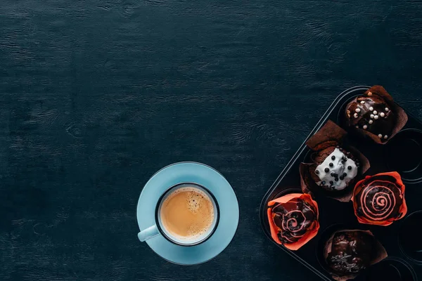 Vista dall'alto di deliziosi muffin con smalto e tazza di caffè blu su sfondo di legno — Foto stock