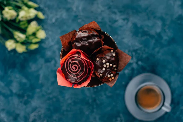 Vista superior de magdalenas dulces con chispas de chocolate y taza de café sobre fondo azul - foto de stock